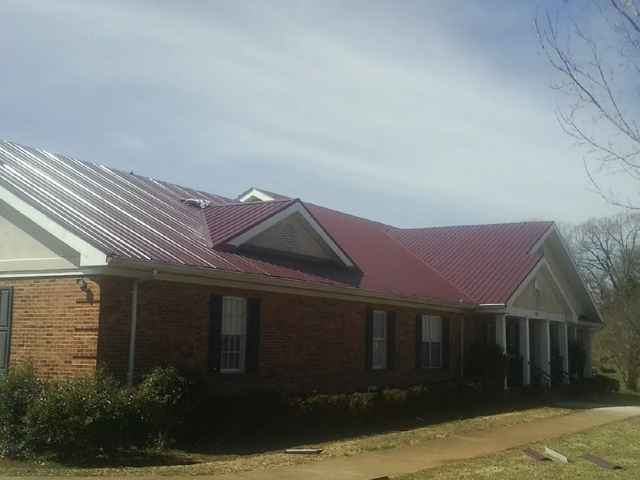 Red metal roof with gabled entries on a long brick building, from a Hail Damage Roof Repair job in High Bridge