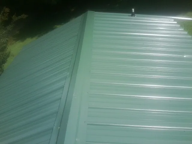 New green metal panels meeting at the ridge of a roof — Flat Roof Repair work by our crew in High Bridge