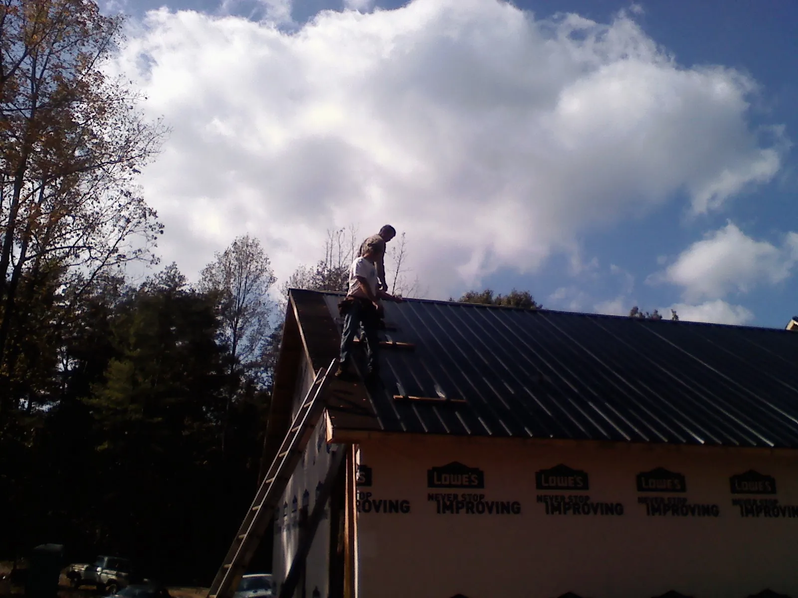 Roofer fastening dark metal panels high against a cloudy sky, from a Roof Inspection job in High Bridge