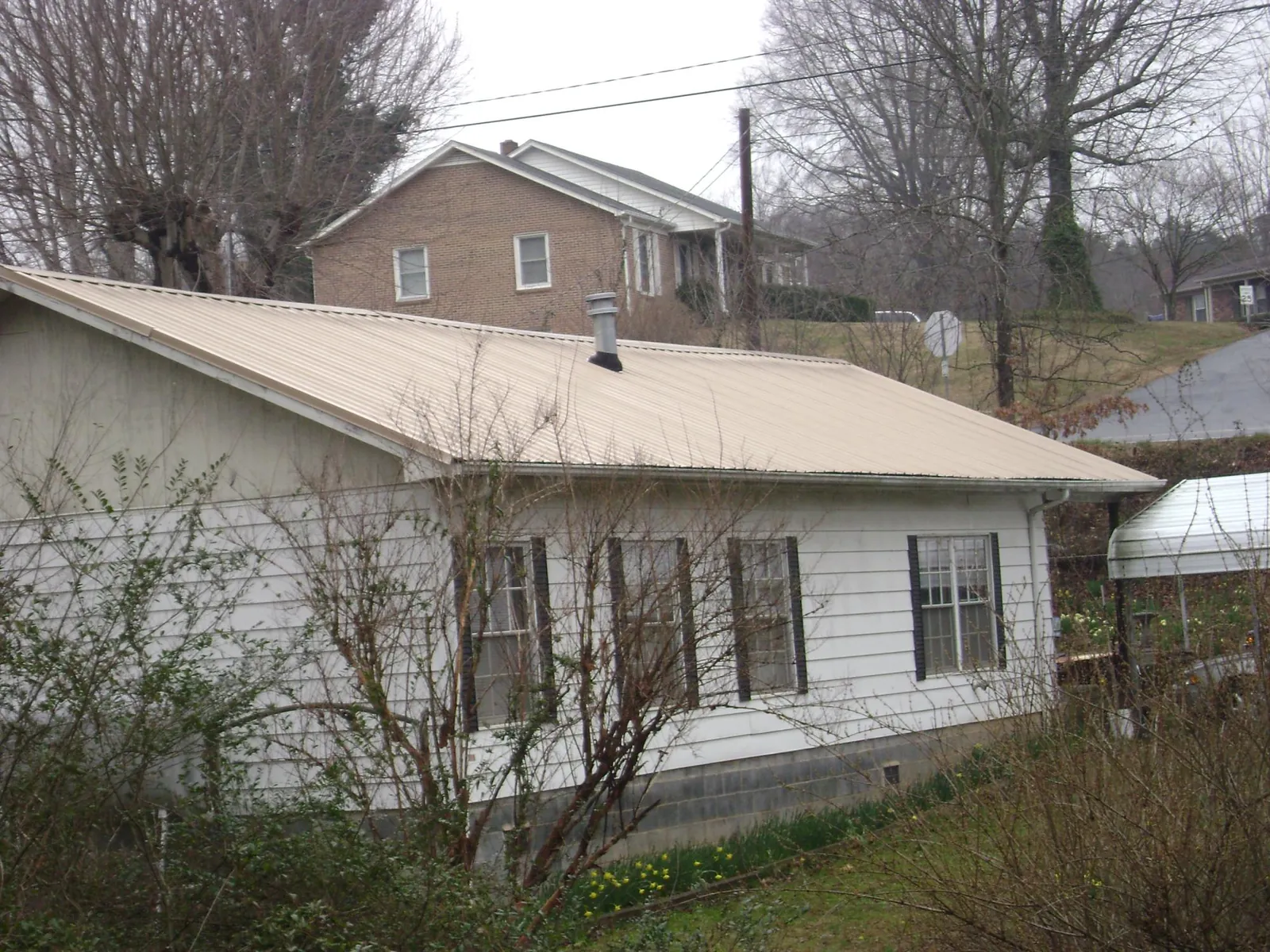 Tan metal roof on a white sided house set into a hillside — Commercial Roofing by Roofing Brothers in High Bridge